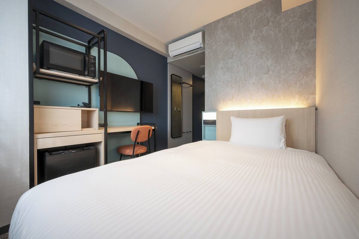 Une chambre d’hôtel équipée d’un lit, d’un bureau avec une chaise, d’un four à micro-ondes, d’un réfrigérateur et d’un appareil de climatisation.
