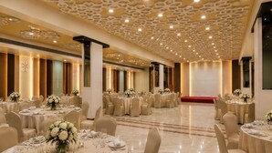 Un salón de banquetes con mesas redondas dispuestas para comer, con un techo que presenta un diseño geométrico e iluminación empotrada.