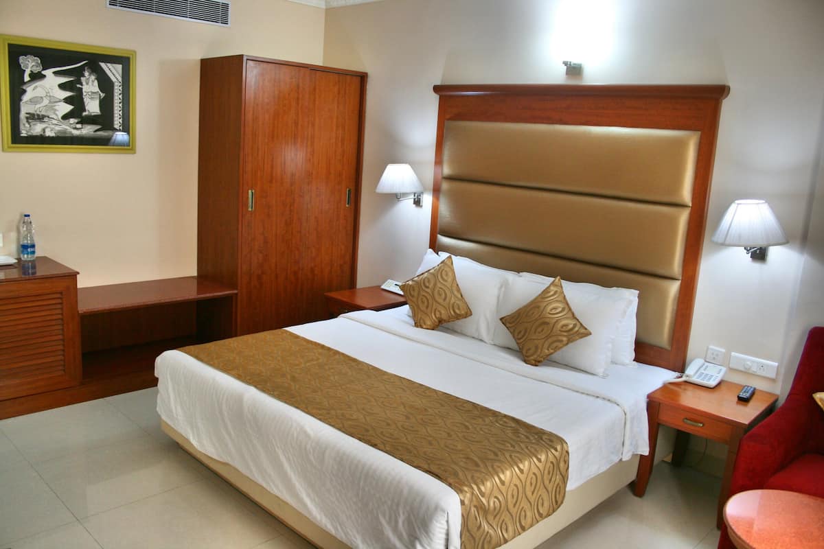 A hotel room with a large bed, wooden wardrobe, bedside lamps, and a red armchair.