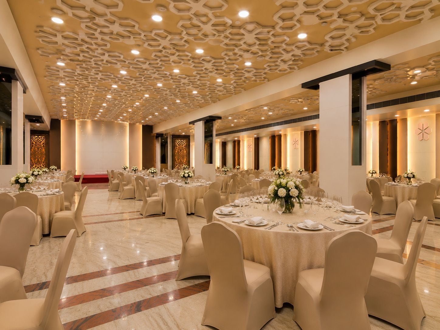 Un salón de banquetes con mesas redondas, sillas color beige y un techo con diseño.