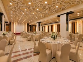 A banquet hall with round tables, beige chairs, and a patterned ceiling.