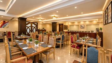 A spacious dining area with multiple tables and chairs, a kitchen area with pots and pans, and a decorative wall with framed artwork.