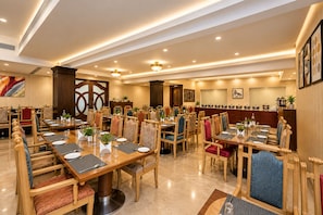 Un comedor amplio con varias mesas y sillas, una zona de cocina con ollas y sartenes, y una pared decorativa con obras de arte enmarcadas.