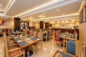 A spacious dining area with multiple tables and chairs, a kitchen area with pots and pans, and a decorative wall with framed artwork.