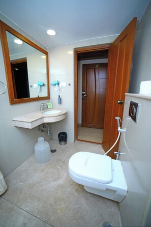 Un baño pequeño con lavamanos, espejo, inodoro y una puerta de madera que da a otra habitación.
