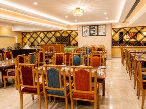 A dining area with multiple tables and chairs, a chandelier, and wall art. - Raj Park Tirupati (Tirupati)