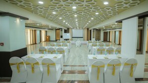 A conference room with white tables and chairs, each with yellow sashes, and a large screen at the front.