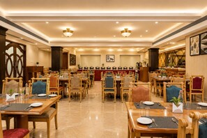 Un restaurante espacioso con varias mesas y sillas, una zona de buffet central y decoración en las paredes.