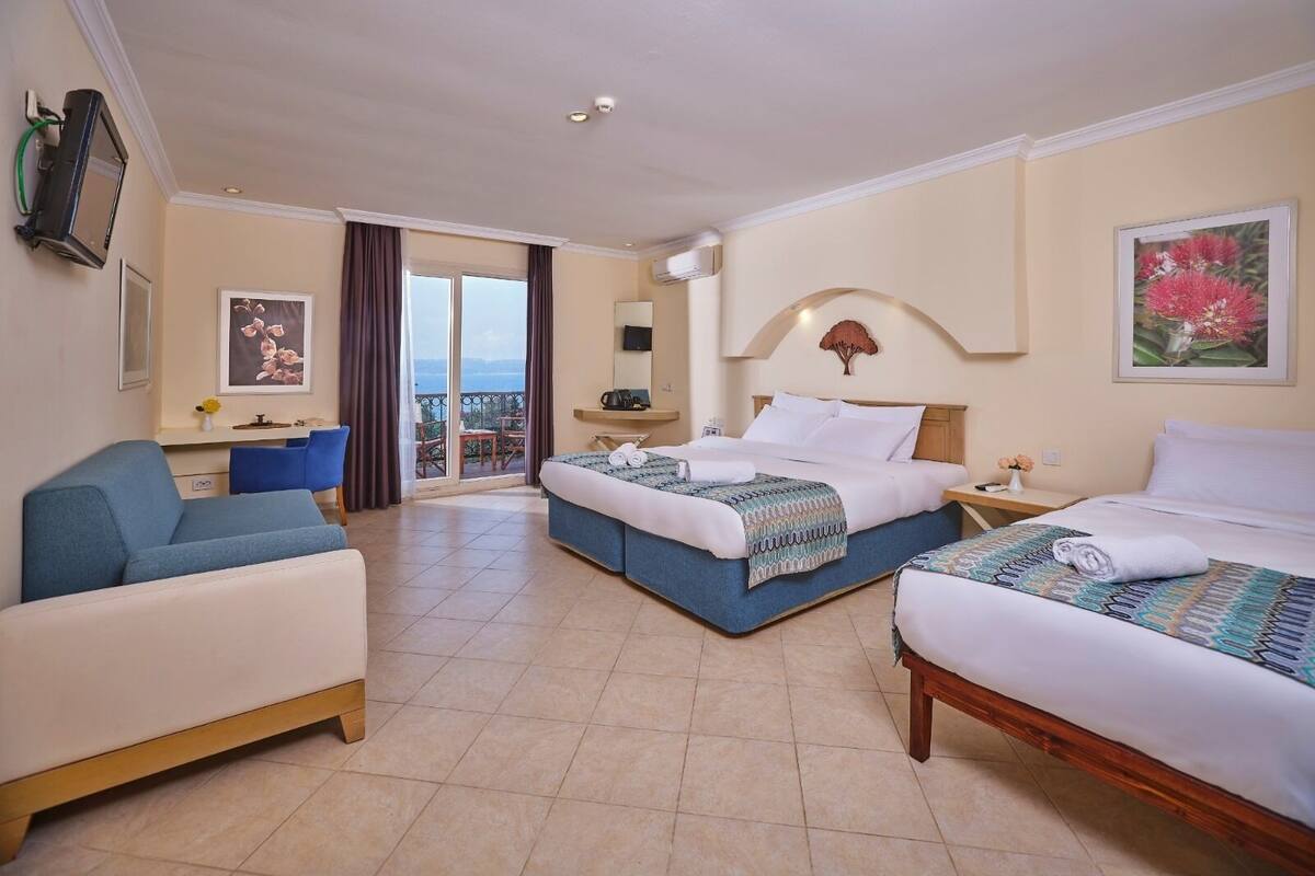 A hotel room with two beds, a sofa, a balcony with a view, and a TV mounted on the wall.