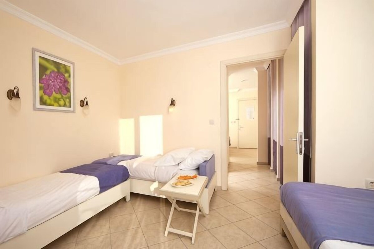 A room with two single beds, a small table with a fruit bowl, and a door leading to another room.