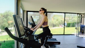 A person using a treadmill in a covered area with large windows, a view of greenery outside, and a Galaxy-branded treadmill.