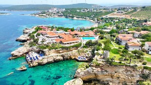 A coastal resort with a rocky shoreline, clear blue waters, and wind turbines in the background.