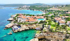 A coastal resort with a rocky shoreline, clear blue waters, and wind turbines in the background.