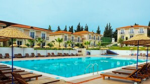 A pool area with sun loungers and umbrellas, surrounded by buildings with balconies.
