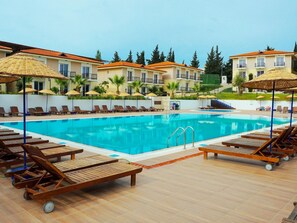 A pool area with sun loungers and umbrellas, surrounded by buildings with balconies.
