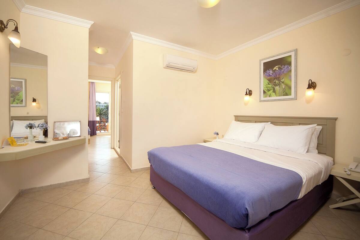A hotel room with a bed, a desk with a mirror, and a picture on the wall.