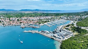 An aerial view of a coastal town with a marina, residential buildings, and surrounding greenery.