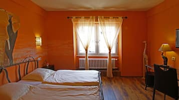 Una stanza con due letti, una finestra con tende, un termosifone, una sedia e una lampada.