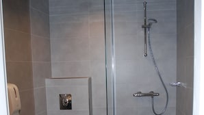 A bathroom with a toilet, a shower with a glass door, and a tiled floor. - Champ'Alsace Centre (Haguenau)