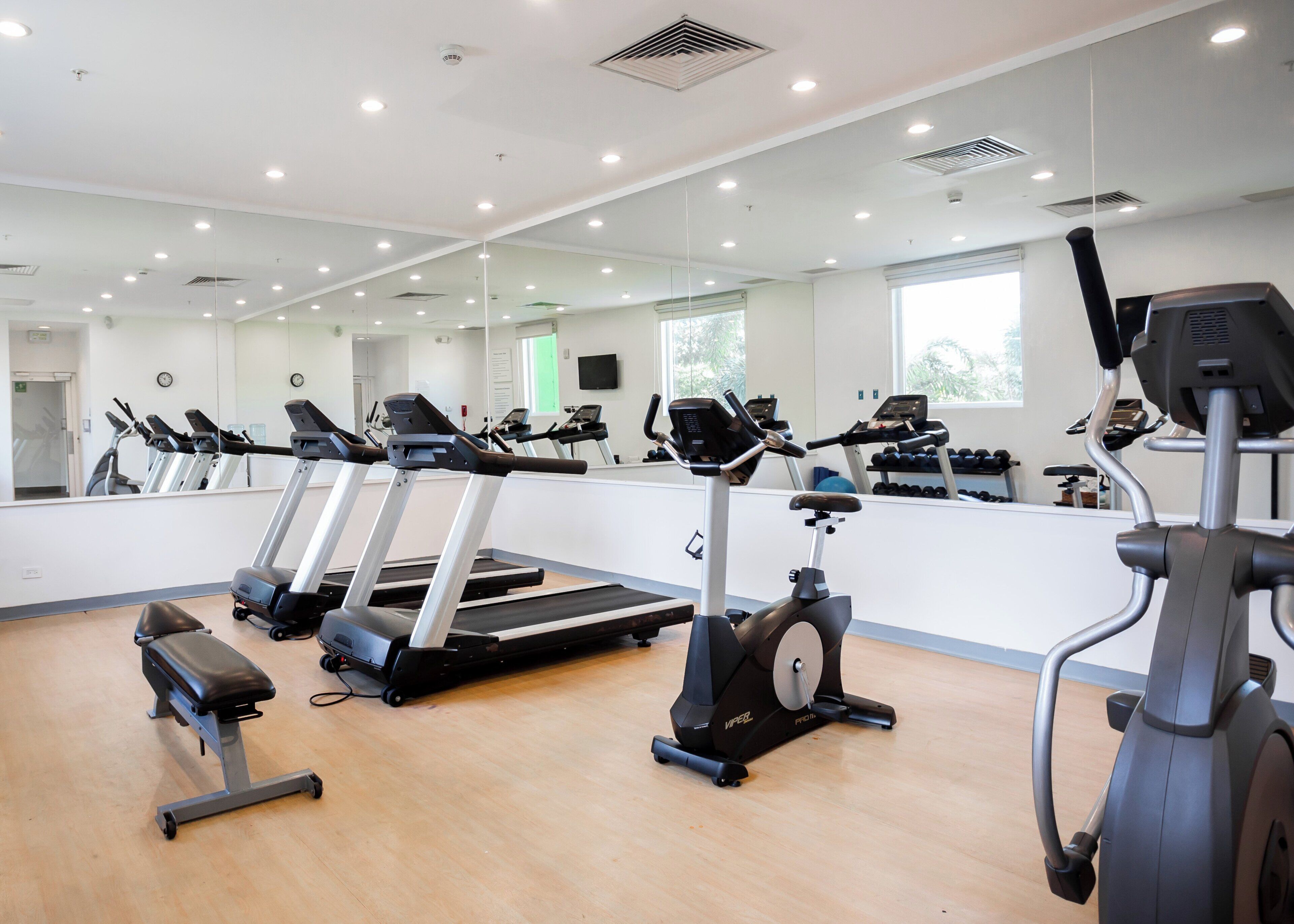 Une salle de sport équipée de plusieurs tapis de course, d’un appareil elliptique et d’un banc de musculation.