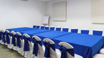 A conference room with a long table, chairs with blue sashes, a whiteboard, and a projector screen.