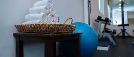 Zona de gimnasio con una cesta de mimbre llena de toallas enrolladas, una pelota de ejercicios azul y equipo de fitness.