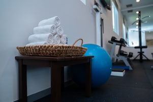 A gym area with a wicker basket of rolled towels, a blue exercise ball, and fitness equipment.