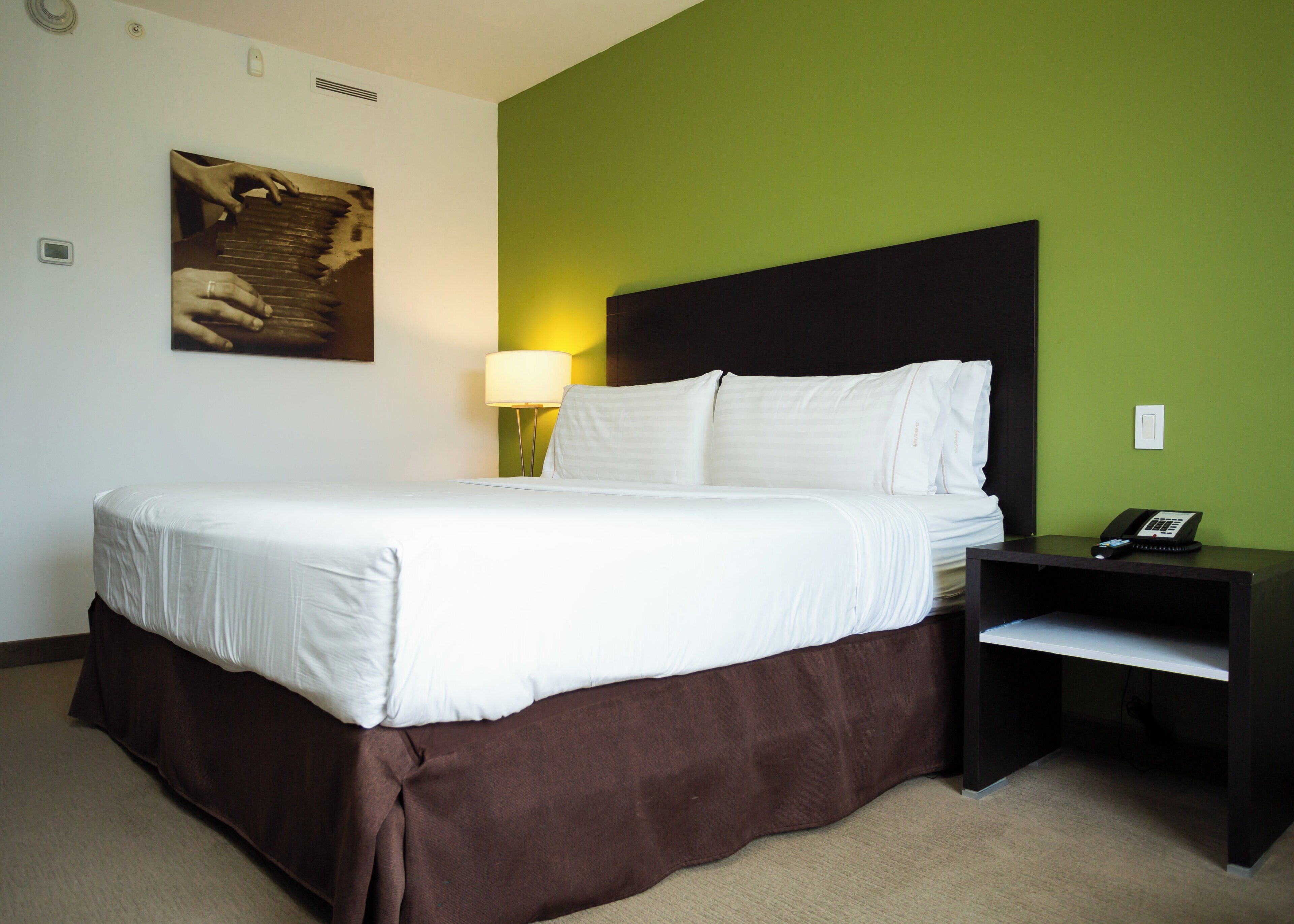 Een hotelkamer met een bed, een nachtkastje met een telefoon en een wandlamp.