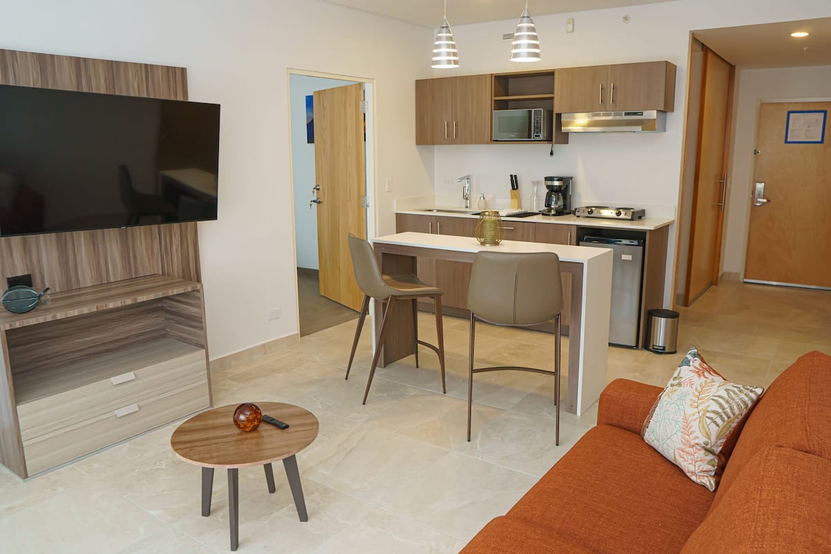 A modern kitchen with a microwave, stove, and sink. There is a dining area with a table and chairs. A flat-screen TV is mounted on the wall.