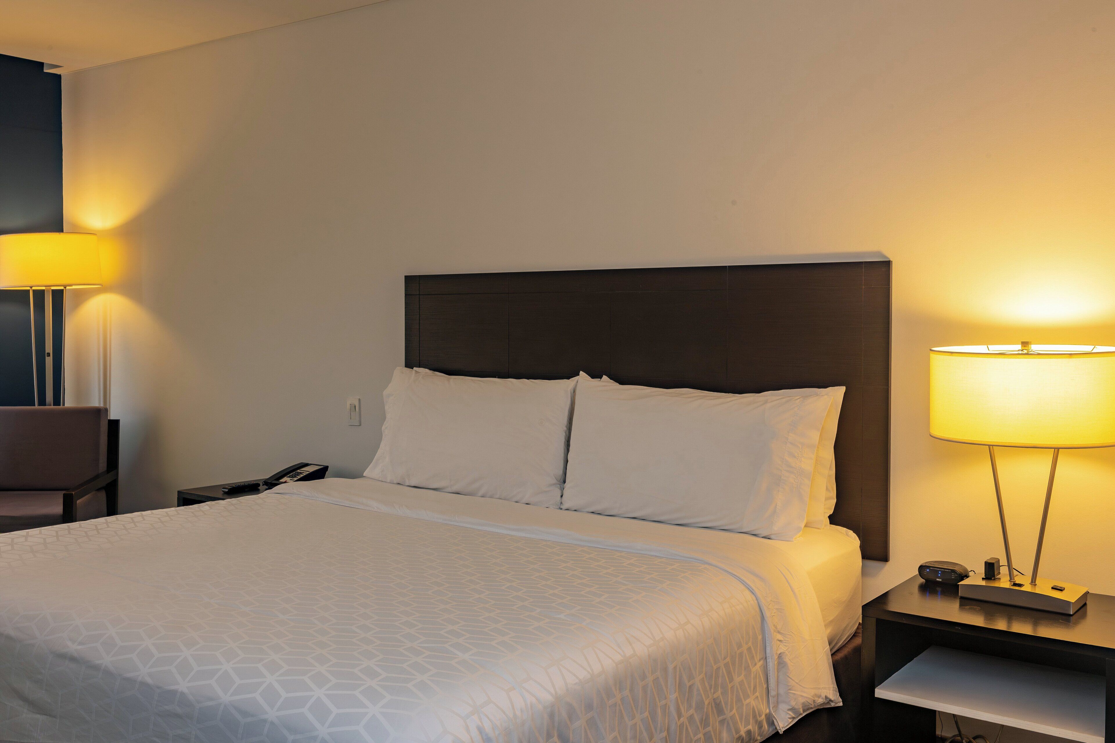 Hotellihuone, jossa on suuri sänky, kaksi yöpöytävalaisinta, yöpöytä ja tuoli.
