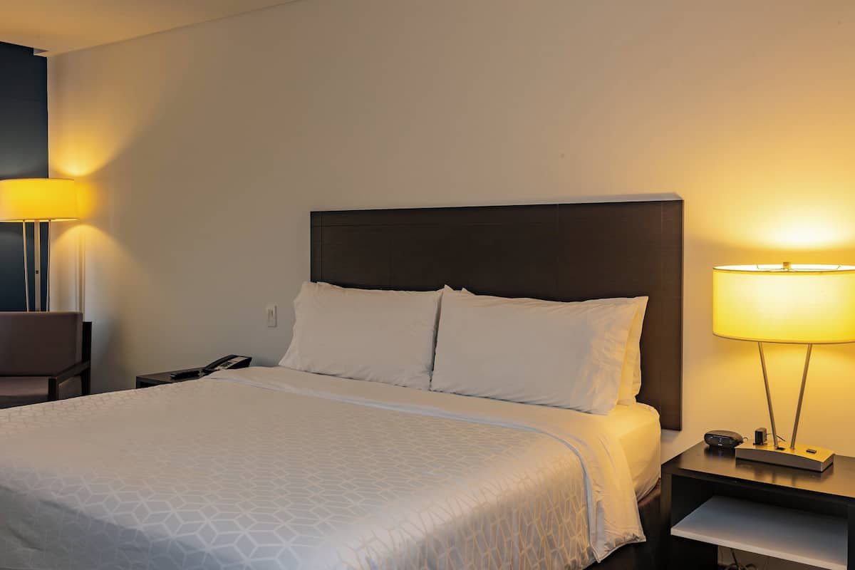 A hotel room with a large bed, two bedside lamps, a nightstand, and a chair.