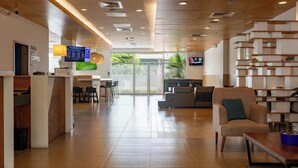 A modern hotel lobby with a reception desk, seating area, and a TV screen displaying the menu. - Holiday Inn Express Managua by IHG (Managua)