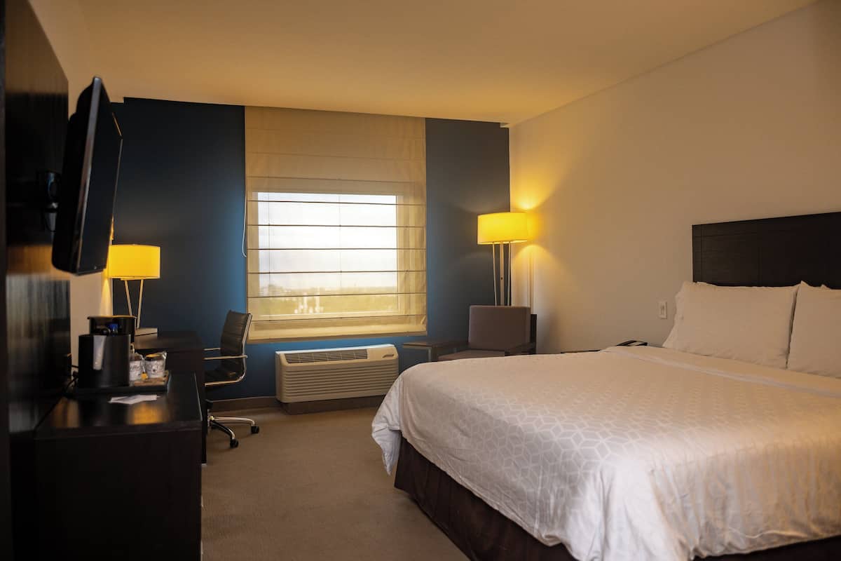A hotel room with a bed, desk, chair, TV, and window with blinds.