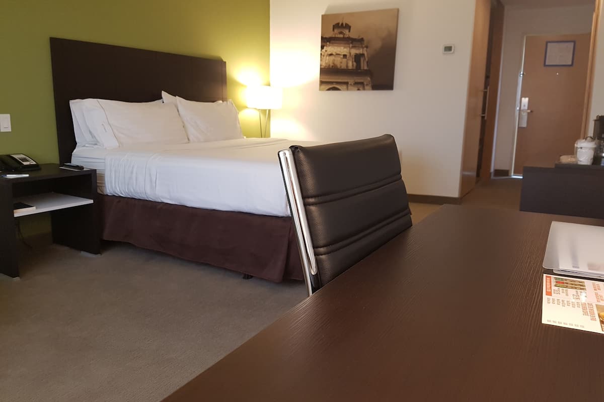 A hotel room with a bed, a nightstand with a phone, a desk with a laptop, and a painting on the wall.