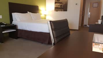 A hotel room with a bed, a nightstand with a phone, a desk with a laptop, and a painting on the wall.