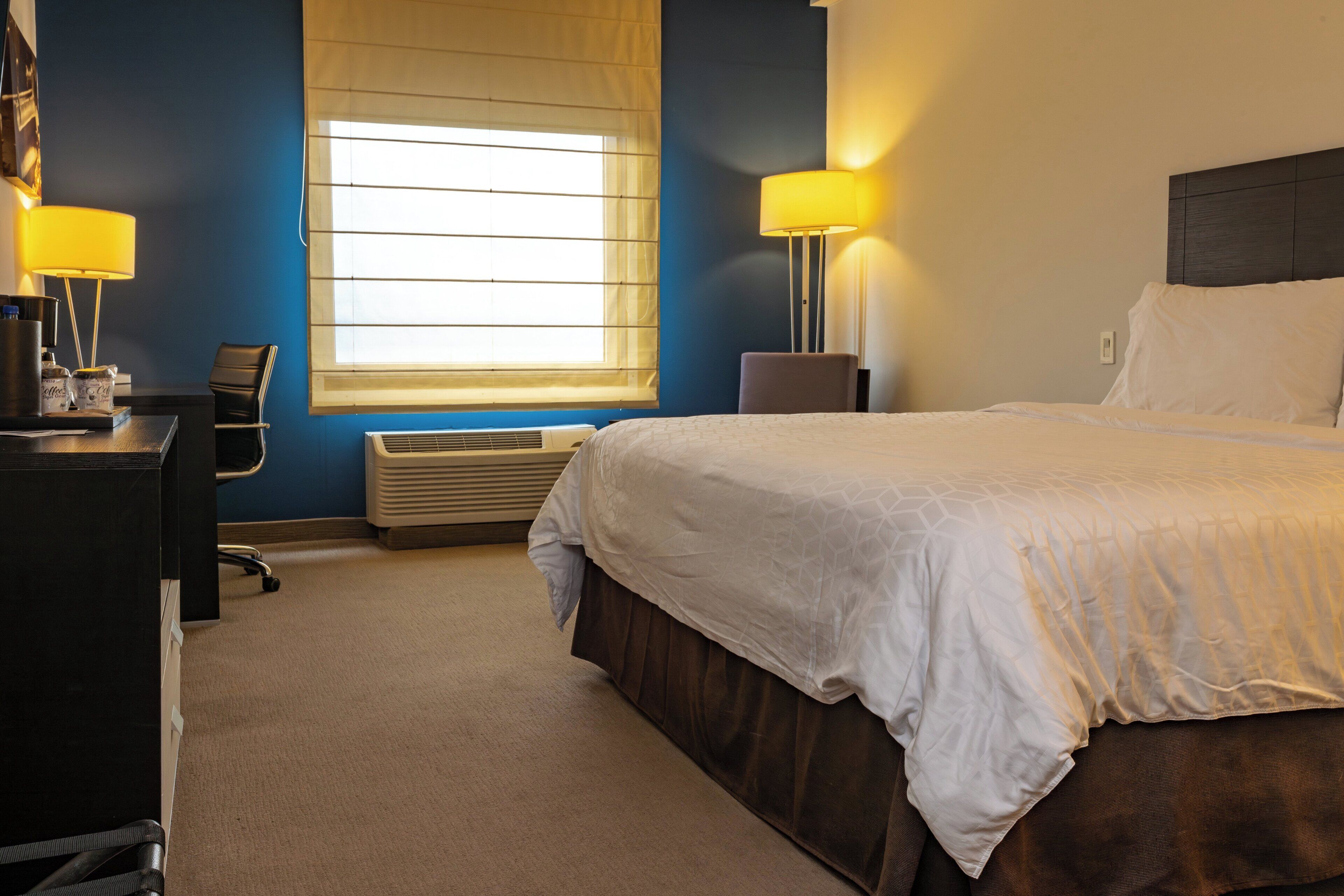 Habitación de hotel con cama, escritorio, silla, lámpara y ventana.