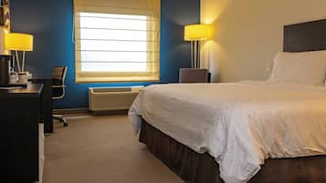 Habitación de hotel con cama, escritorio, silla, lámpara y ventana.