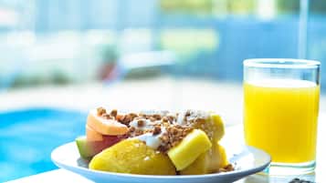 Een fruitsalade met granola en een glas sinaasappelsap op een tafel naast een zwembad.