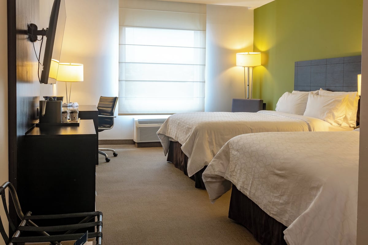 A hotel room with two beds, a desk, a chair, and a window with blinds.