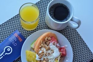 A breakfast setting with a plate of fruit, a glass of orange juice, and a cup of coffee on a woven placemat.