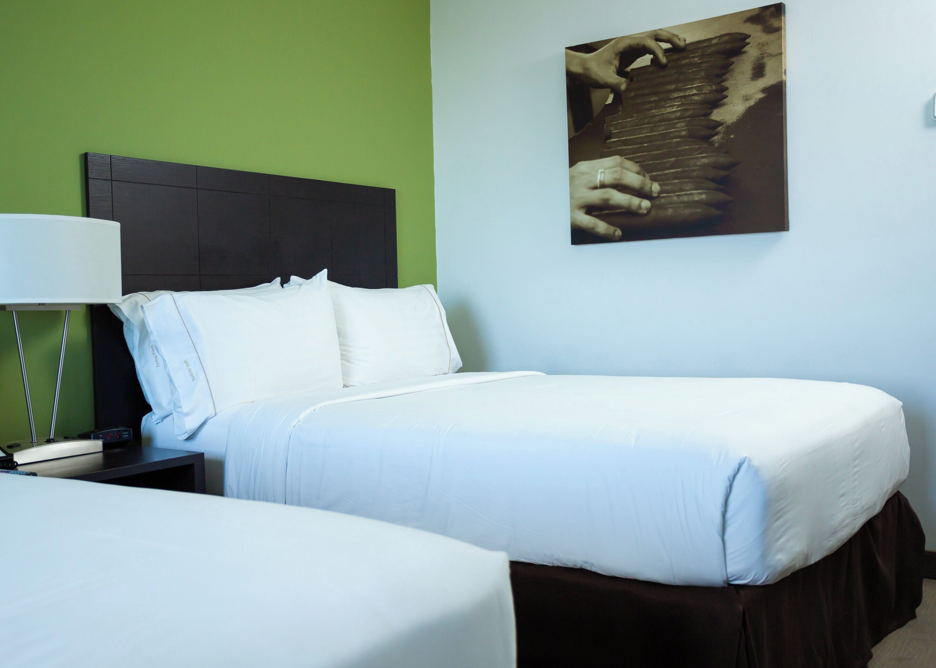 A hotel room with a bed, a nightstand, a lamp, and a painting on the wall.