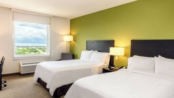 A hotel room with two beds, a desk, a chair, and a window with a view.
