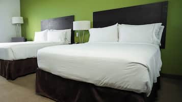 A hotel room with two beds, a green wall, and a dark headboard.
