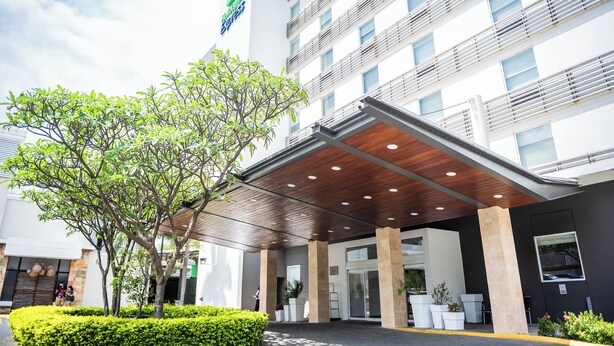 A modern hotel entrance with a covered walkway, large windows, and a prominent logo on the building. - Holiday Inn Express Managua by IHG (Managua)
