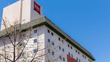 Edifício de hotel com logotipo vermelho e branco bem visível, várias janelas e céu azul.