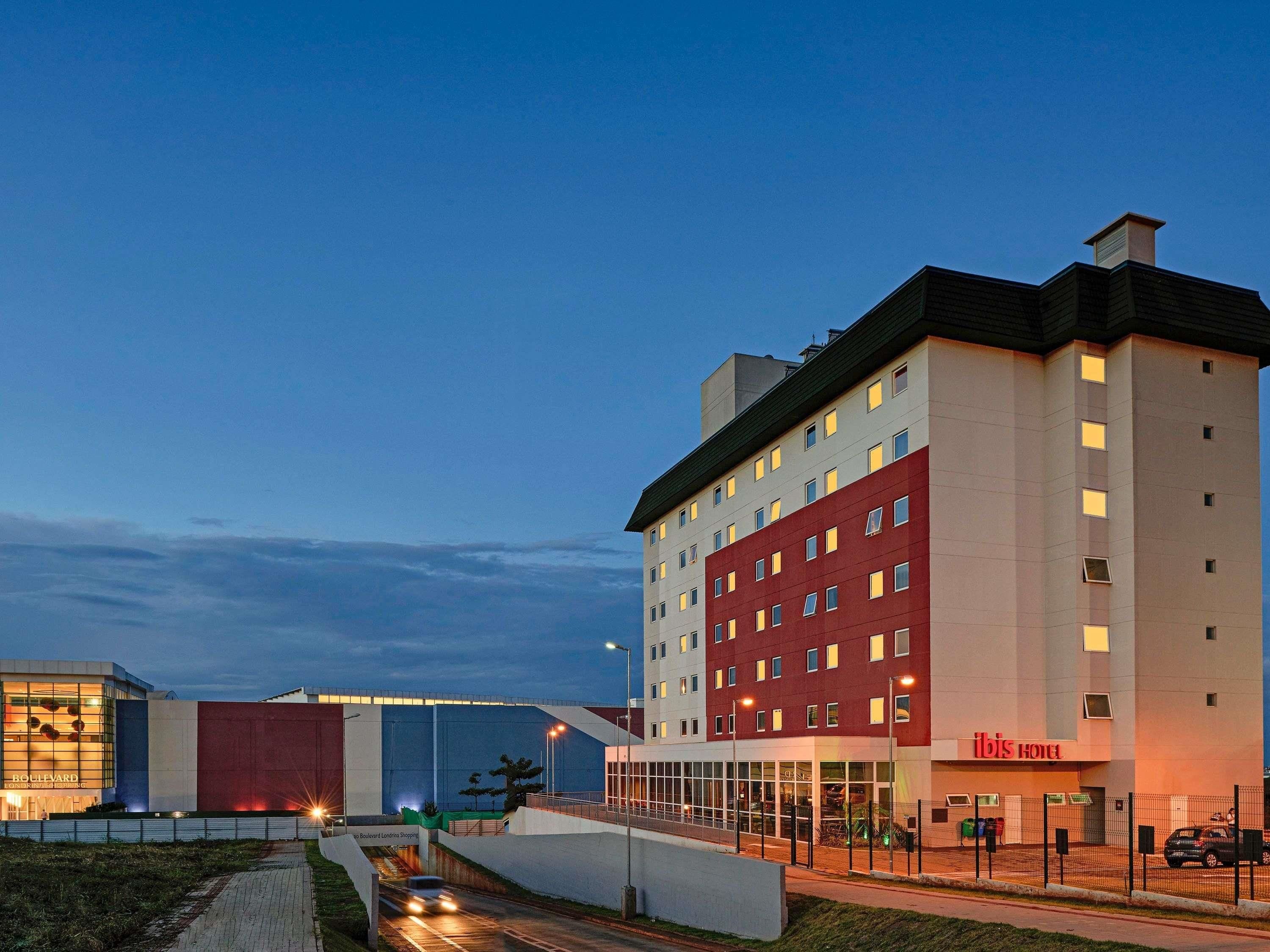 Un hotel con varios pisos, una fachada roja destacada y una entrada de vidrio amplia.