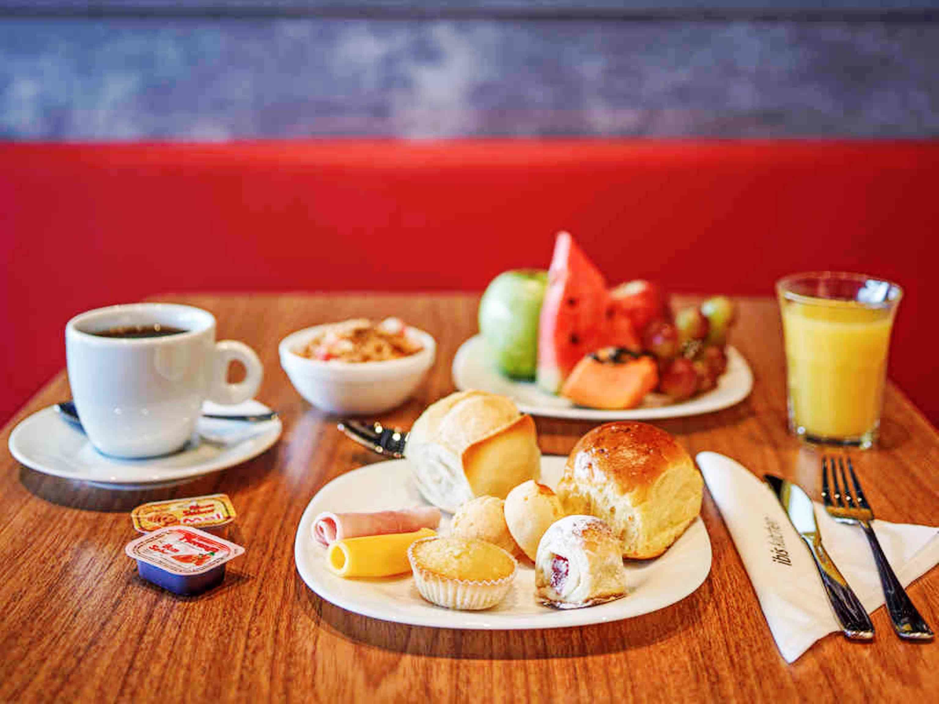 Una escena de desayuno con una taza de café, un tazón de cereal, un plato con pastelería, un vaso de jugo de naranja y un plato de fruta.