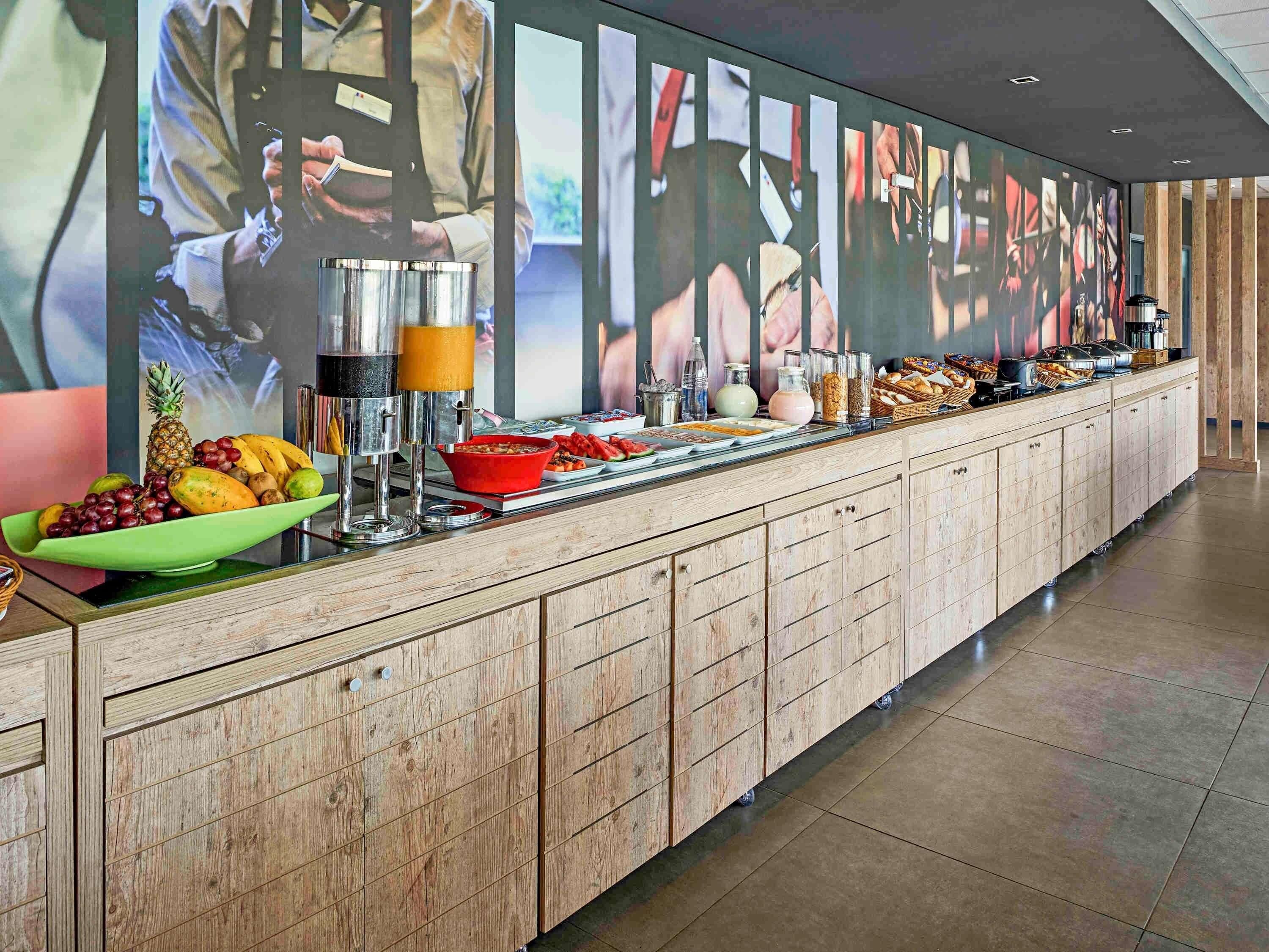 A buffet setup with a variety of food items and beverages, a green bowl of fruits, and a coffee machine.