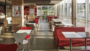 A modern restaurant interior with a long counter, red upholstered booths, and a view through large windows. - ibis Londrina Shopping (Londrina)
