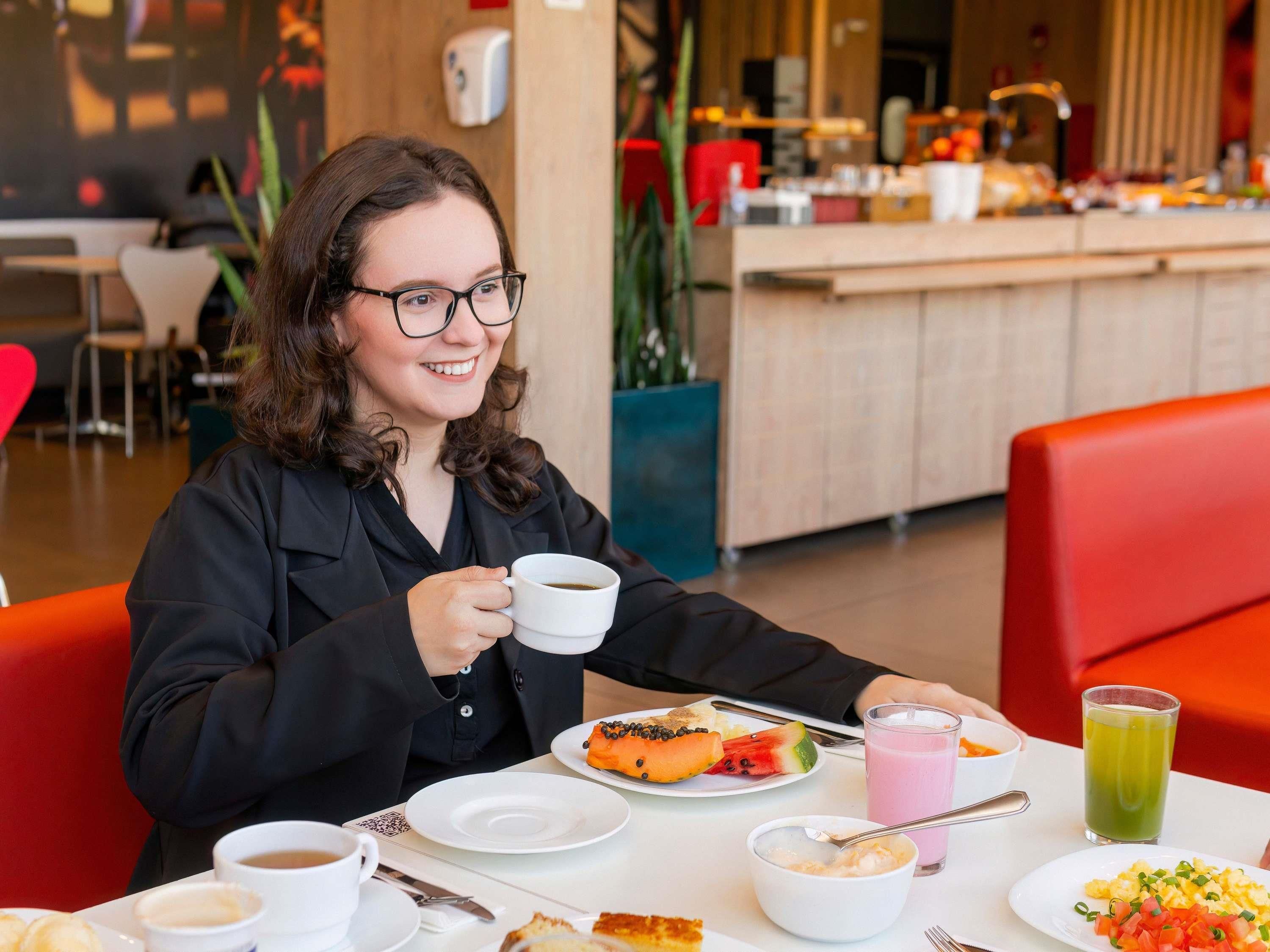 Uma pessoa sentada à mesa com uma xícara de café, um prato de comida e um copo de suco.